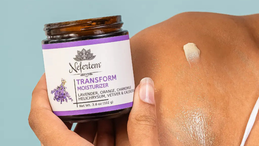 Person applying Nefertem Transform Moisturizer to their skin with a blue background