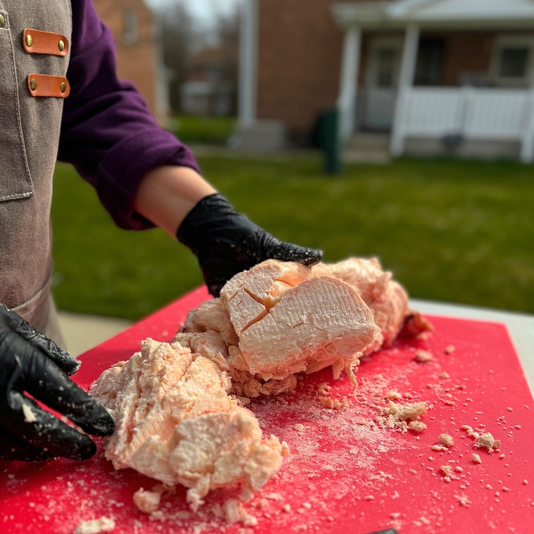 Person handling raw beef suet on a red cutting board outdoors