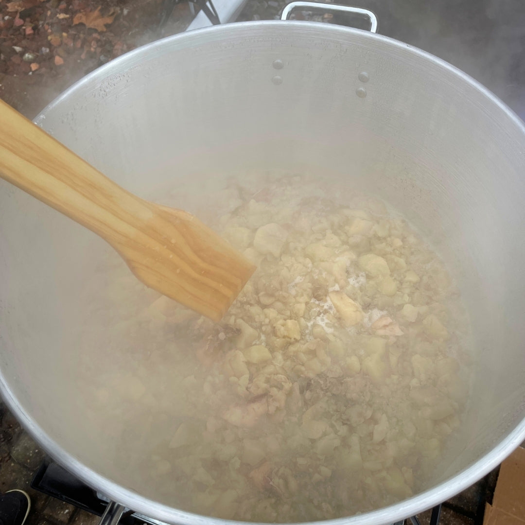 Large pot with beef suet being stirred with a wooden spoon on a stove.