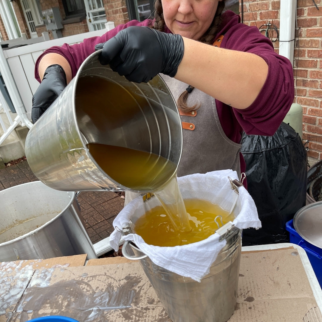 Person pouring tallow from a metal container into a bag outdoors.